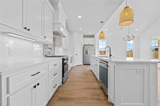 kitchen with white cabinets, sink, hanging light fixtures, an island with sink, and stainless steel appliances