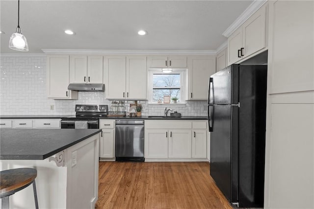 kitchen with a sink, under cabinet range hood, appliances with stainless steel finishes, dark countertops, and backsplash