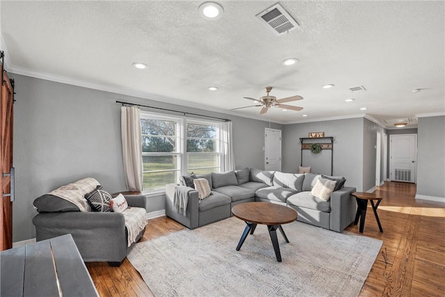 living room featuring visible vents, hardwood / wood-style flooring, a textured ceiling, crown molding, and baseboards