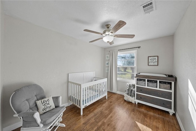 bedroom with visible vents, a crib, baseboards, wood finished floors, and a ceiling fan