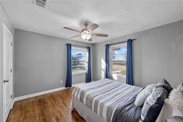 bedroom featuring visible vents, ceiling fan, baseboards, wood finished floors, and a textured ceiling