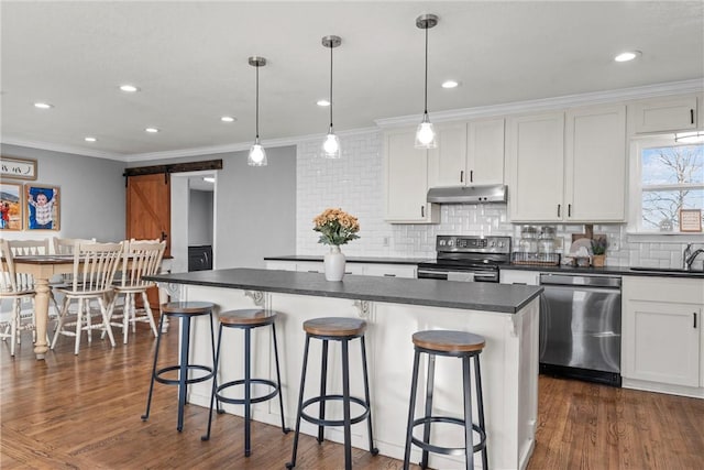 kitchen with under cabinet range hood, dark countertops, a kitchen island, stainless steel appliances, and a barn door