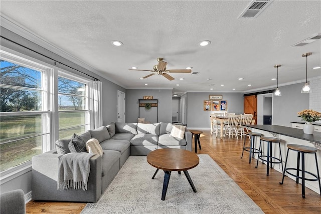 living area with visible vents, a barn door, recessed lighting, a textured ceiling, and crown molding