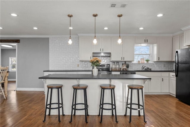 kitchen with visible vents, stainless steel range with electric stovetop, under cabinet range hood, dark countertops, and freestanding refrigerator