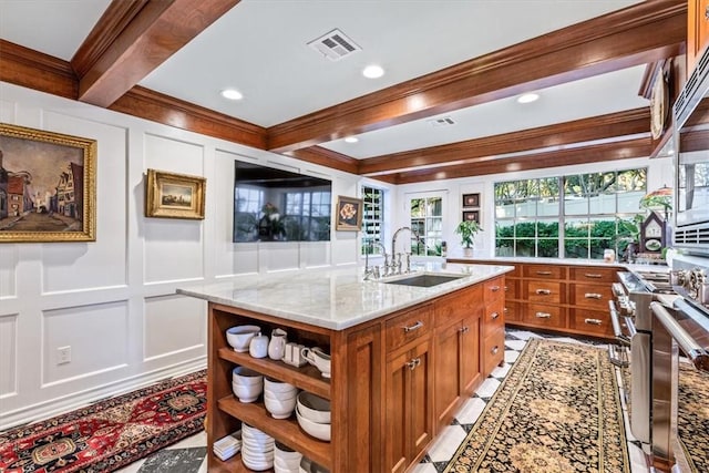 kitchen with light stone counters, sink, a center island with sink, and ornamental molding