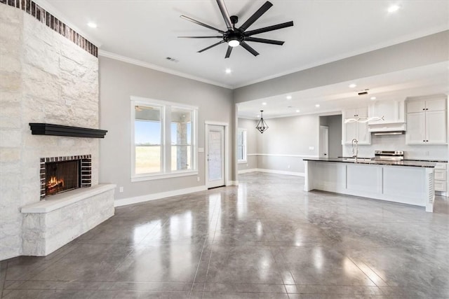 unfurnished living room with concrete flooring, ceiling fan, crown molding, sink, and a fireplace