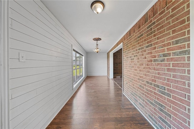 hall featuring dark wood-type flooring, brick wall, and an inviting chandelier