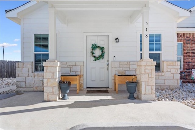 view of exterior entry featuring stone siding and fence