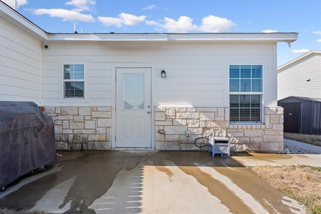 doorway to property with stone siding and a patio