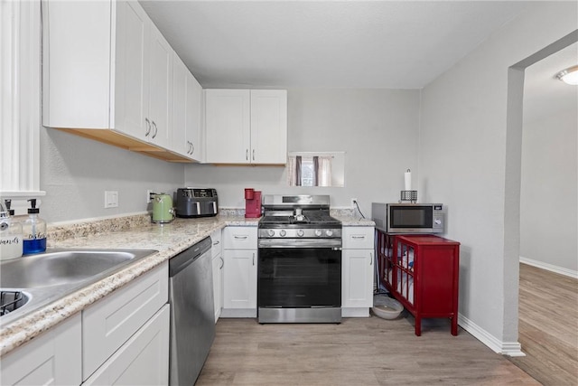 kitchen with baseboards, white cabinets, stainless steel appliances, light wood-type flooring, and a sink