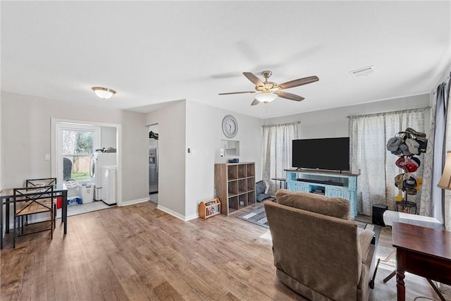 living room featuring washer / dryer, baseboards, visible vents, a ceiling fan, and wood finished floors