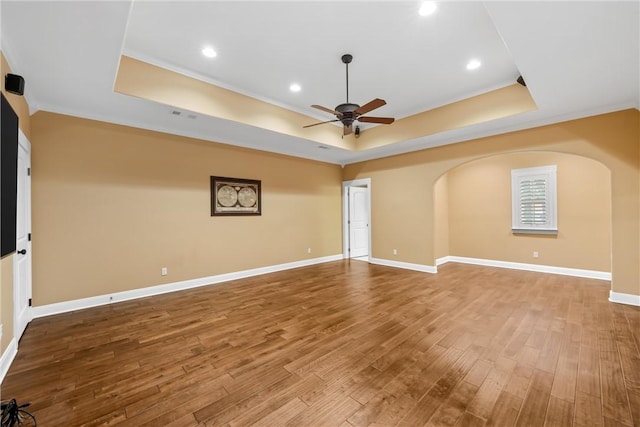 empty room with a tray ceiling, ceiling fan, wood-type flooring, and ornamental molding