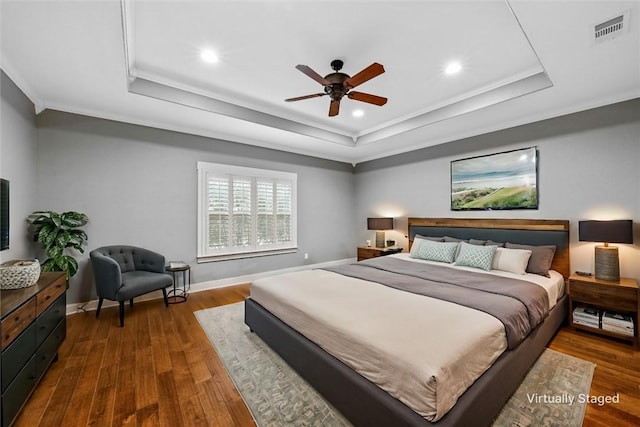 bedroom with ceiling fan, a raised ceiling, dark wood-type flooring, and crown molding