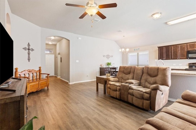 living area featuring arched walkways, lofted ceiling, ceiling fan with notable chandelier, baseboards, and light wood finished floors