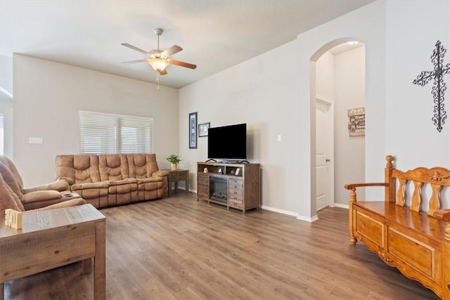 living room featuring arched walkways, ceiling fan, baseboards, and light wood-style floors