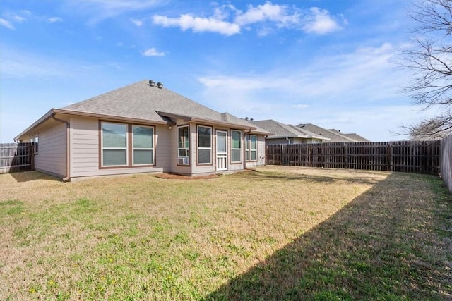 rear view of property featuring a shingled roof, a lawn, and a fenced backyard