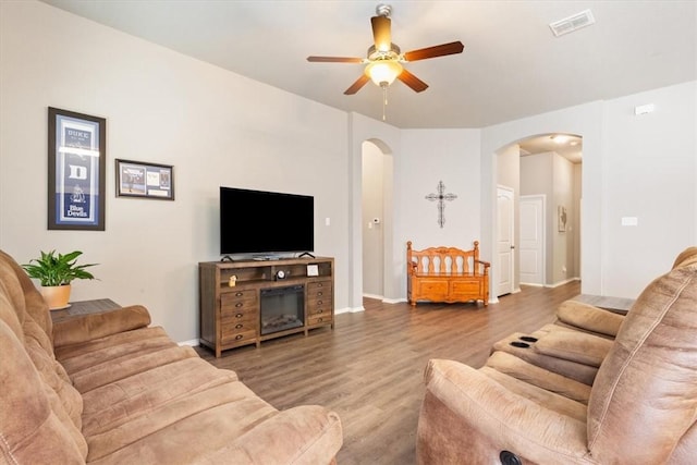 living room featuring arched walkways, ceiling fan, wood finished floors, visible vents, and baseboards