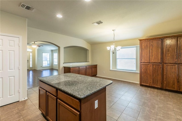 kitchen featuring dark stone counters, ceiling fan with notable chandelier, light tile patterned floors, decorative light fixtures, and a kitchen island