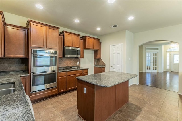 kitchen with french doors, backsplash, stainless steel appliances, and dark stone countertops