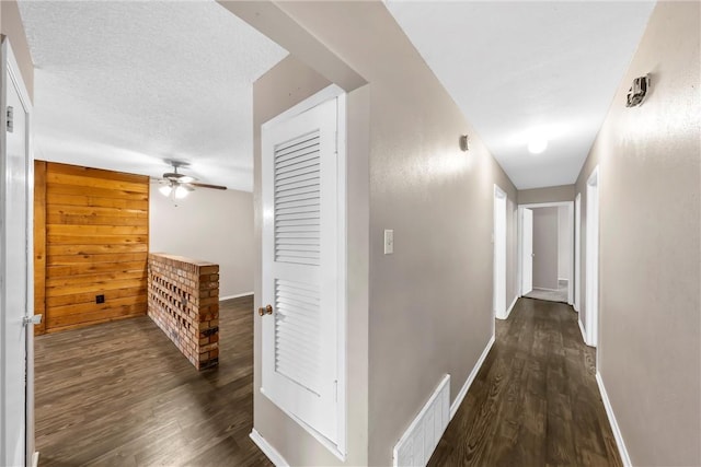 hall with a textured ceiling, wooden walls, and dark hardwood / wood-style floors