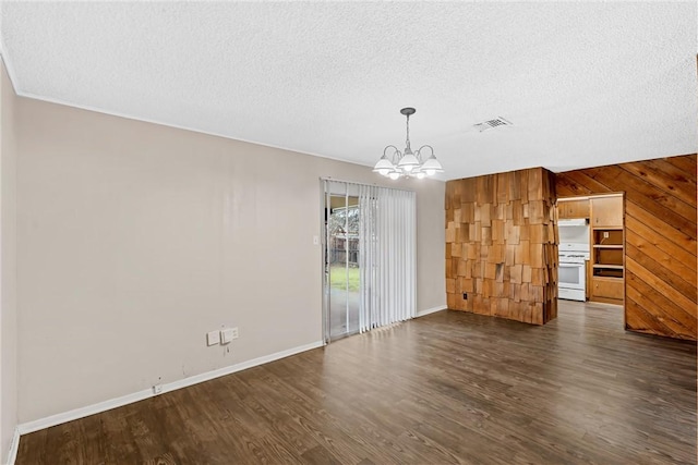 unfurnished dining area featuring dark wood-type flooring, an inviting chandelier, wooden walls, and a textured ceiling