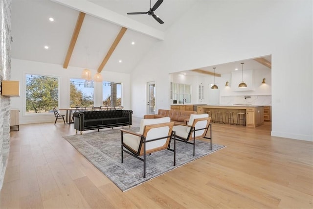 living room featuring ceiling fan with notable chandelier, beam ceiling, high vaulted ceiling, light hardwood / wood-style floors, and a stone fireplace