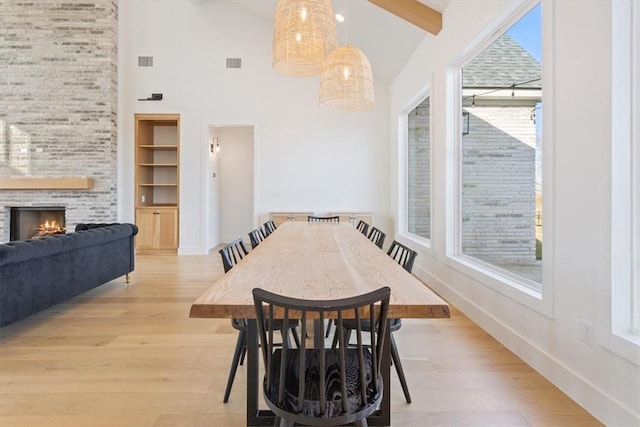 dining area with a fireplace, beam ceiling, light hardwood / wood-style floors, and high vaulted ceiling