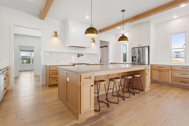 kitchen with stainless steel fridge, white cabinetry, a kitchen island, and beam ceiling