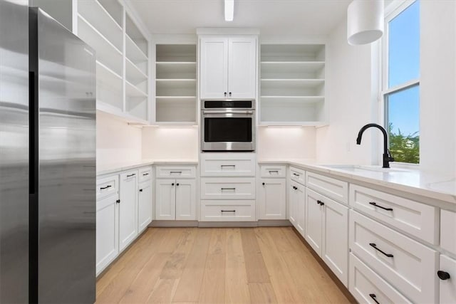 kitchen with light stone countertops, white cabinetry, sink, stainless steel appliances, and light wood-type flooring