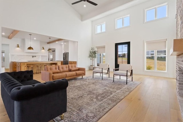 living room featuring a high ceiling, light wood-type flooring, ceiling fan, and beam ceiling