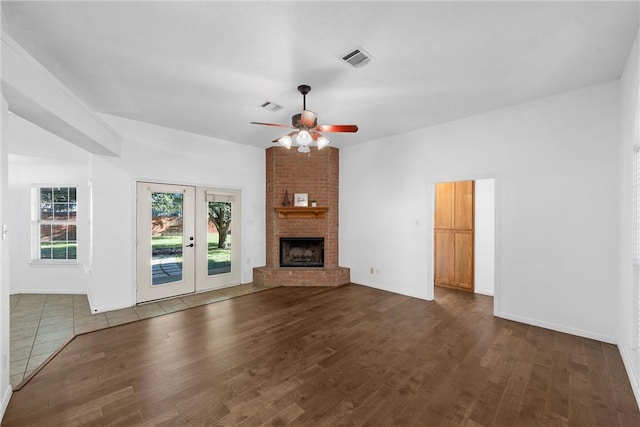 unfurnished living room with a brick fireplace, ceiling fan, dark hardwood / wood-style flooring, and french doors