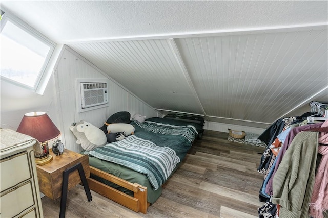 bedroom featuring lofted ceiling with skylight, a wall unit AC, and wood finished floors