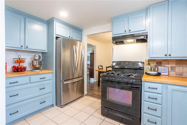 kitchen featuring blue cabinetry, butcher block counters, freestanding refrigerator, black range with gas cooktop, and under cabinet range hood