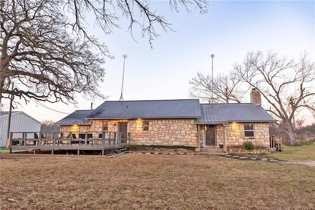 rear view of property with a lawn, stone siding, a chimney, metal roof, and a wooden deck