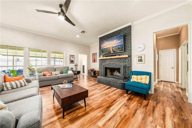 living room featuring ceiling fan, wood-type flooring, ornamental molding, and a brick fireplace