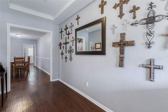 hall with a tray ceiling, wood-type flooring, and a textured ceiling