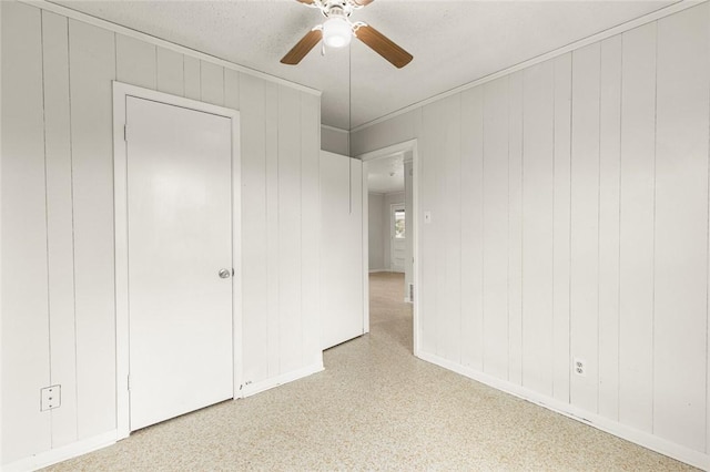 unfurnished bedroom featuring ceiling fan, wood walls, and a textured ceiling