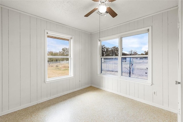 unfurnished room with a textured ceiling, ceiling fan, and wood walls