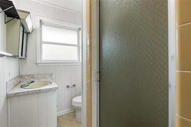 bathroom with vanity, wooden walls, toilet, and a shower with shower door