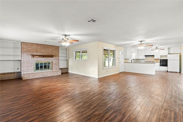 unfurnished living room with ceiling fan, a fireplace, dark wood-type flooring, and a textured ceiling