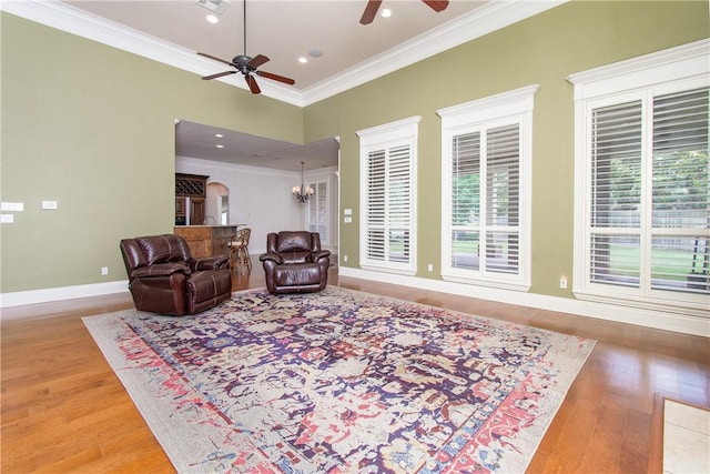 living room with hardwood / wood-style floors, ceiling fan with notable chandelier, a healthy amount of sunlight, and ornamental molding