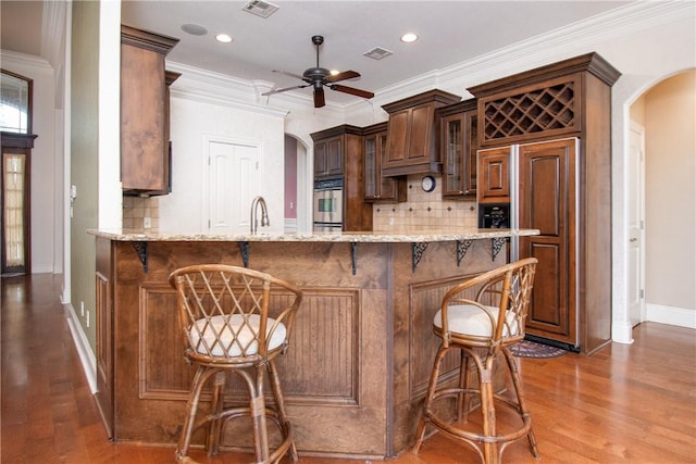 kitchen with decorative backsplash, kitchen peninsula, stainless steel oven, ceiling fan, and wood-type flooring