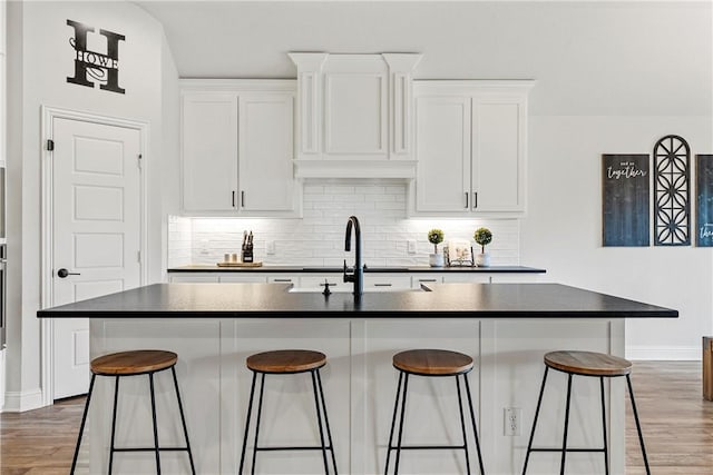 kitchen with dark countertops, decorative backsplash, white cabinets, a sink, and a kitchen breakfast bar