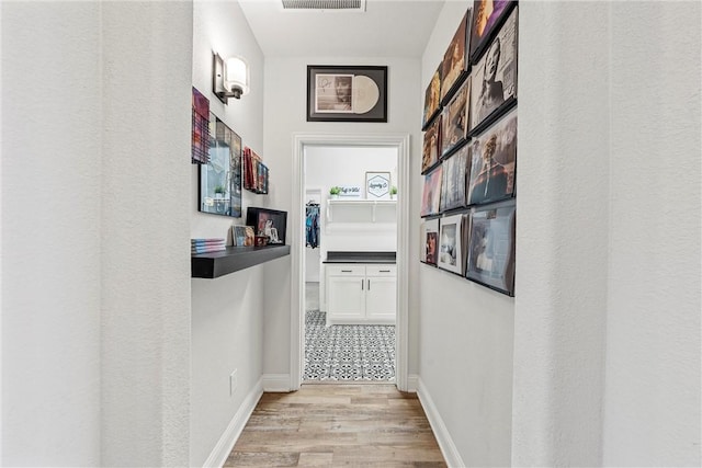 hallway featuring light wood finished floors, visible vents, and baseboards