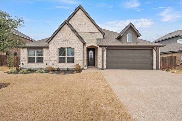 french country style house featuring driveway, roof with shingles, fence, and brick siding