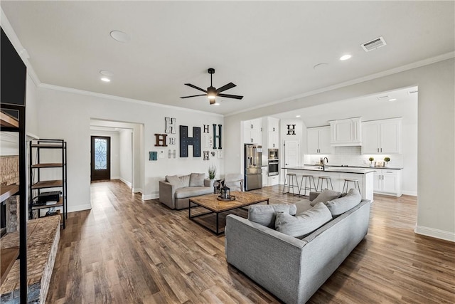 living area with ceiling fan, wood finished floors, visible vents, baseboards, and crown molding