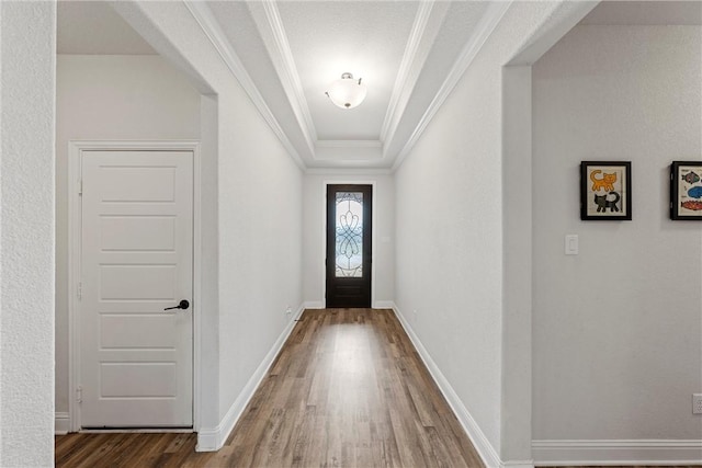 doorway to outside with baseboards, a tray ceiling, dark wood finished floors, and crown molding