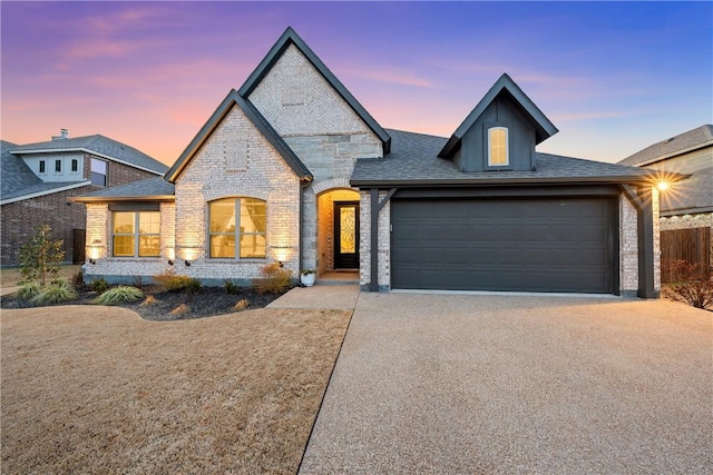 french country home with driveway, stone siding, a shingled roof, and brick siding