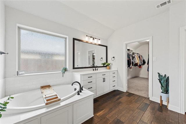 full bathroom featuring visible vents, a spacious closet, vaulted ceiling, vanity, and wood finished floors