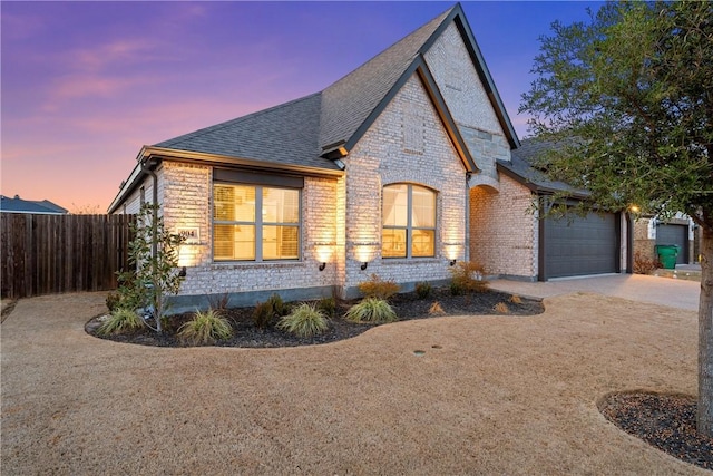 view of front of property with roof with shingles, brick siding, an attached garage, fence, and driveway